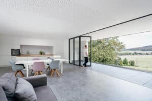 Ein Balkon mit geöffneter Glas‑Faltwand, die nahtlos in eine helle Wohnküche übergeht, von Solarlux.
