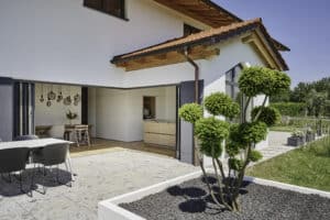 Ein großzügiger Garten mit Terrasse, die durch eine vollständig geöffnete Glas‑Faltwand mit dem Innenraum verbunden ist — von Solarlux.