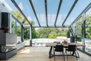 Terrassenüberdachung bzw. Wintergarten mit mit anthrazitfarbener Rahmenkonstruktion, Glasschiebewtüren, Kamin und geneigtem Glasschiebedach von Solarlux.