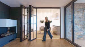 Modernes Wohnzimmer mit Durchgang zur Küche und Glas-Faltwand in Sprossenoptik mit schwarzem Rahmen von SOLARLUX.
