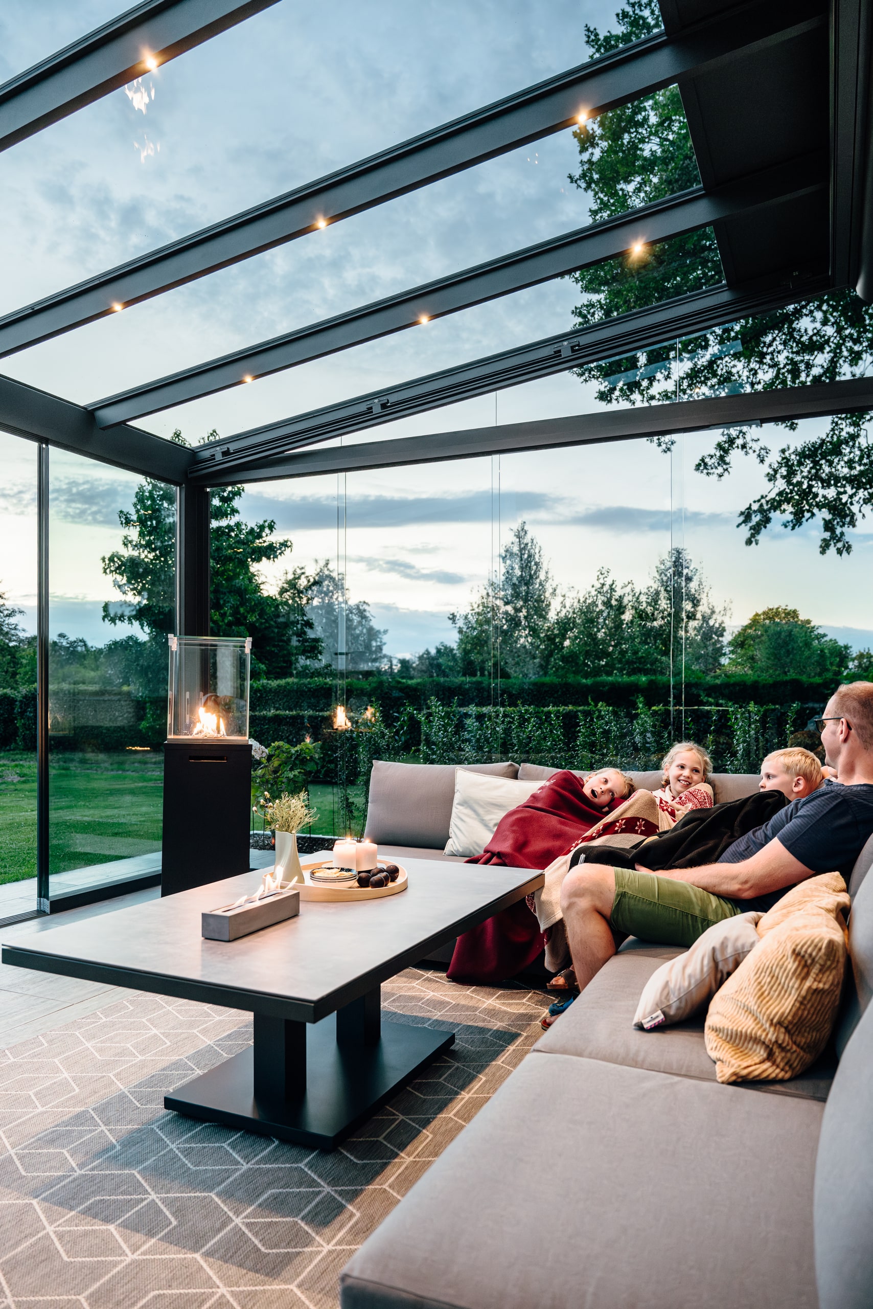 Eine Familie genießt entspannt den warmen Sommerabend im modernen Glashaus von Solarlux.