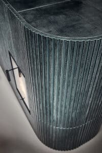 Detailaufnahme eines Kamins mit abgerundeten Aussenkanten, Relief-Keramik in Stäbchen-Optik in einem Blau bzw. Petrolton mit besonderer Glasurmusterung und Kamintüre mit Sichtfenster von Sommerhuber.