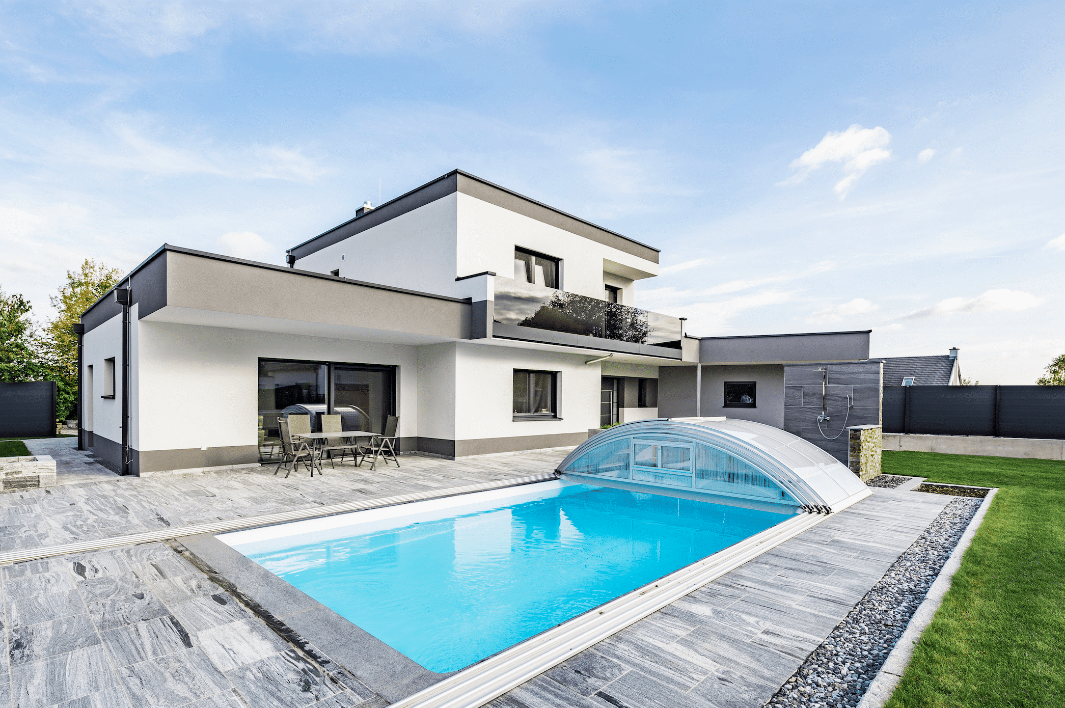 SynthesaGruppe zeigt ein Einfamilienhaus mit Flachdach, überdachtem Pool, verglasten Balkon und einer gefliesten Terrasse mit einer Sitzgruppe.