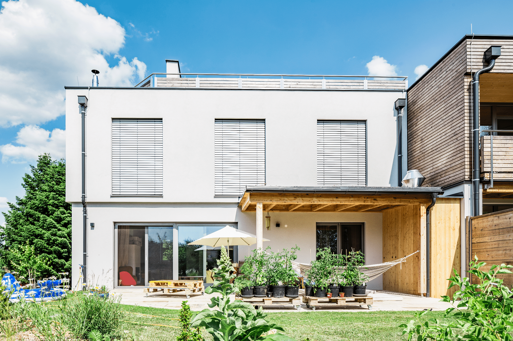 SynthesaGruppe zeigt ein Einfamilienhaus mit einer überdachten Terrasse und Holzverkleidung , große Fenster mit Rollläden und einem modernen Flachdach.