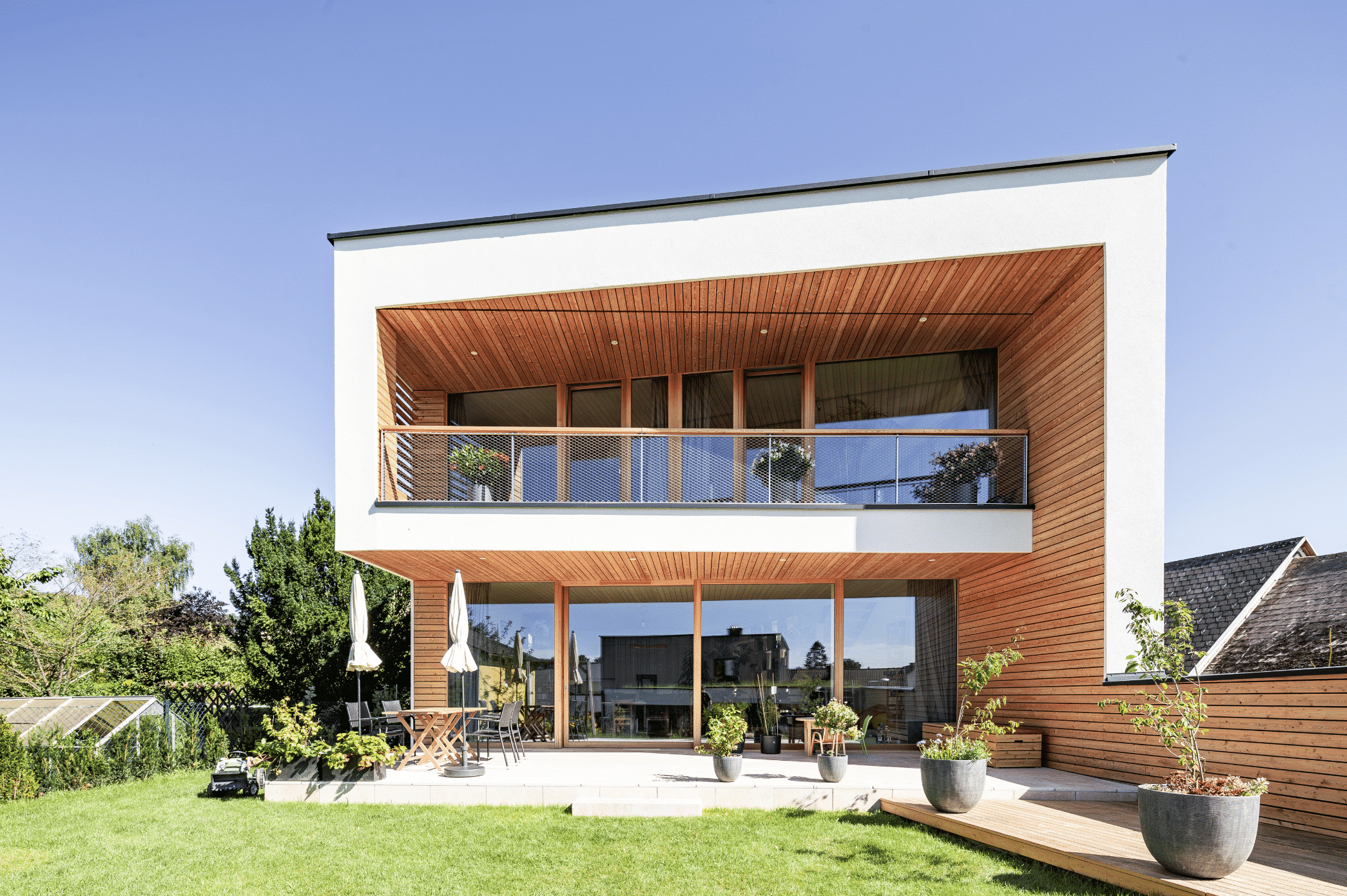 Modernes Einfamilienhaus mit Holzverkleidung und Schrägdach mit einer überdachten Terrasse, einer Sitzgruppe und Sonnenschirmen von SynthesaGruppe.