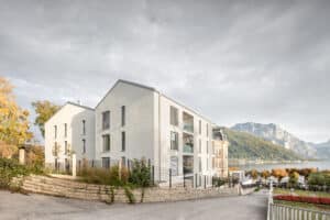 Synthesagruppe zeigt ein Mehrparteienhaus mit Satteldach, großen Fenstern und weißer Fassade.
