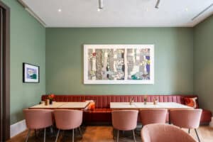 Synthesagruppe zeigt das Referenzprojekt Hotel Sans Souci in Wien. Ein Speisesaal mit grüner Wandfarbe und Sitzgelegenheiten mit orangem Leder- und Stoffbezug.