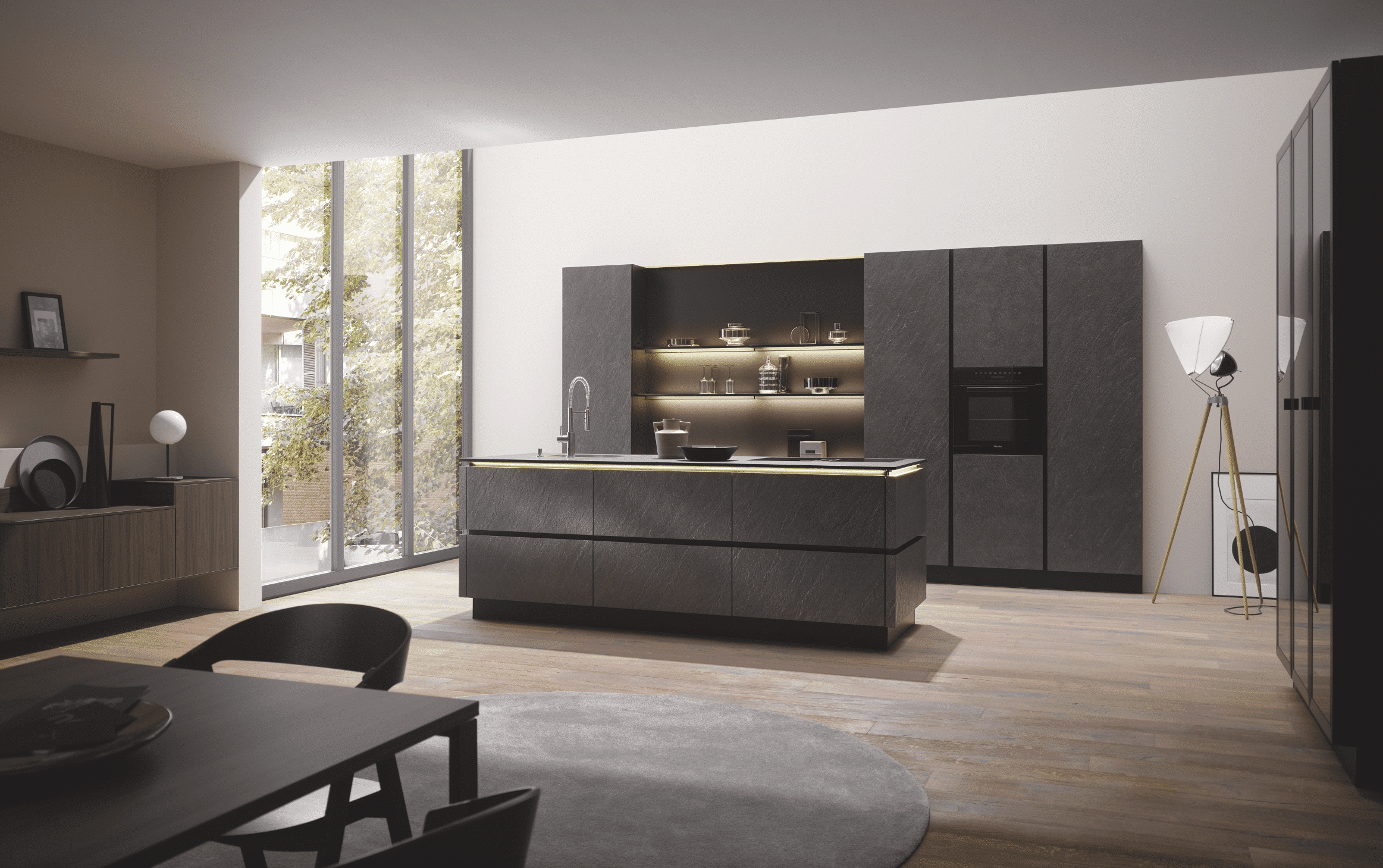 Bauer Tischlerei zeit eine moderne Küche mit Holzboden und einer Kücheninsel in dunklem grau mit Spülbecken und großem Einbauschrank mit integriertem Backofen von Häcker Küchen.