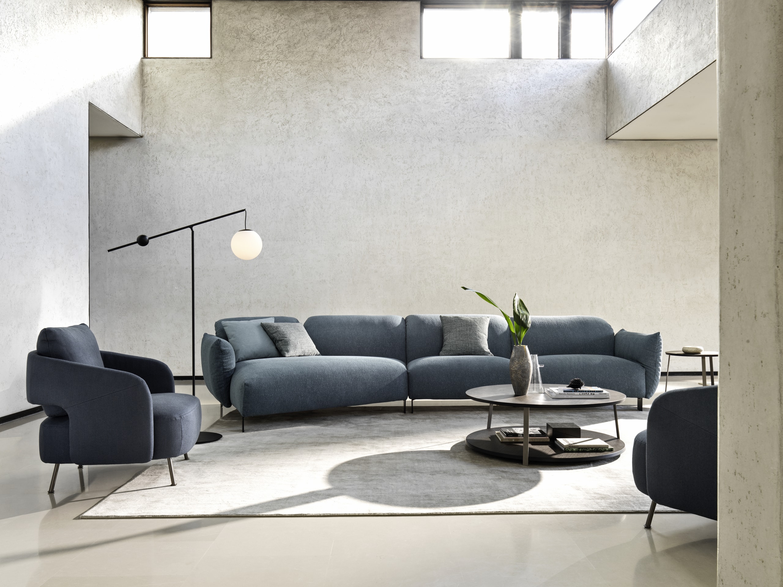 Bauer Tischlerei präsentiert Wohnlandschaft bestehend aus einer leicht gebogenen Couch mit dunkelblauem Stoffbezug und zwei bequemen Sesseln mit Armlehne von Ditre Italia.
