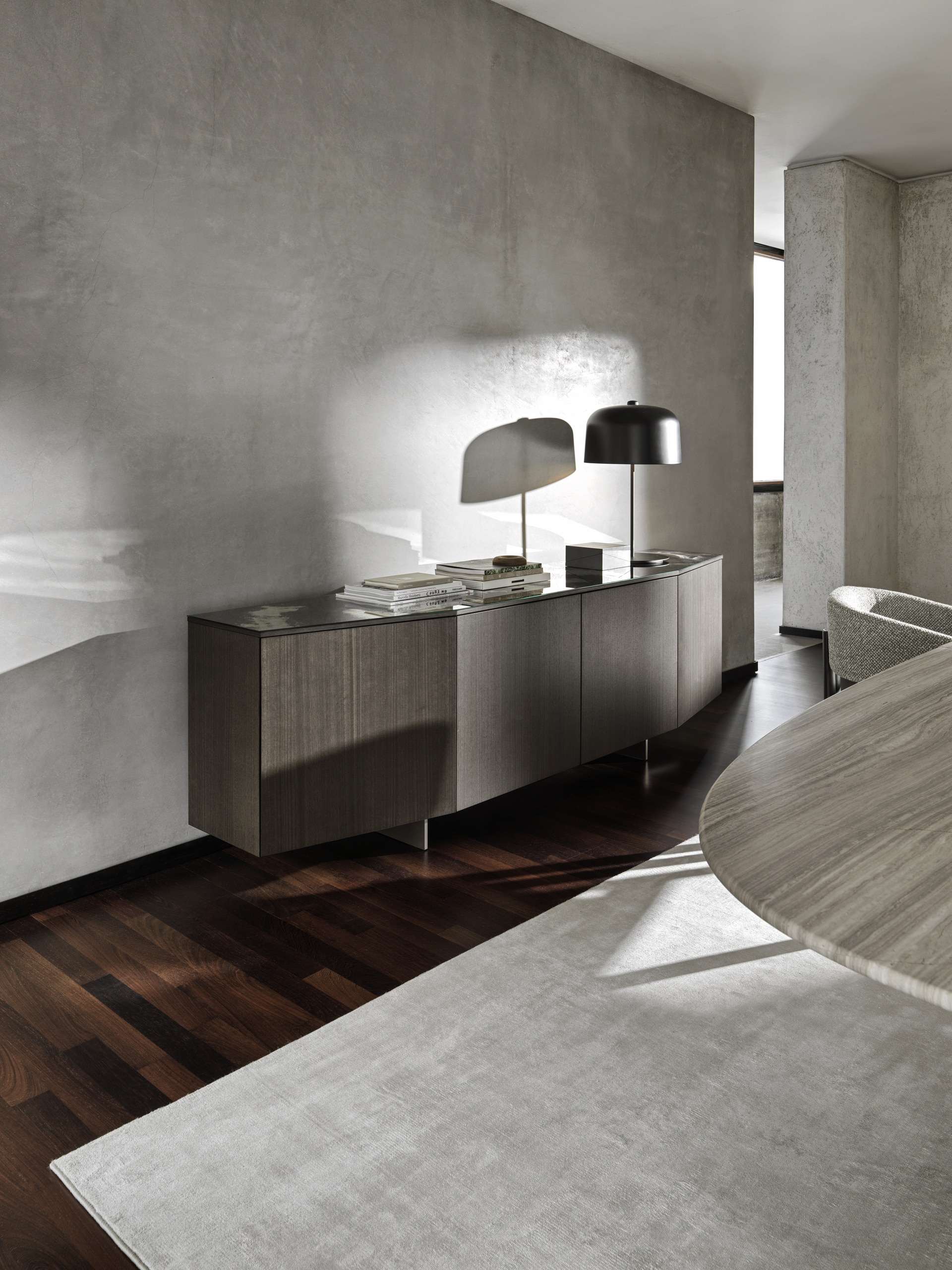 Bauer Tischlerei zeigt Sideboard aus dunklem Holz in gebogener Optik mit fünf grifflosen Türen und Glasplatte an der Oberseite von Ditre Italia.