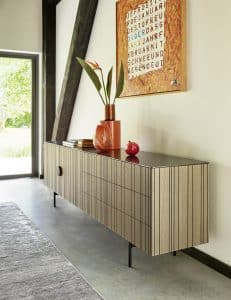 Bauer Tischlerei zeigt Sideboard mit griffloser gerillter Holzfront und glänzender schwarz marmorierten Abstellfläche von haas Möbelwerk.