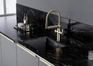 BAUER Tischlerei zeigt eine BLANCO ausziehbare Armatur mit Soda-Funktion in Gold und Anthrazit auf schwarzer Marmorarbeitsplatte, passend zu den Küchenfronten und Beschlägen.