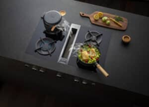BAUER Tischlerei zeigt den BORA Professional Gasherd mit integriertem silbernen Downdraft-Abzug in einer hochwertigen Küche mit dunkler Steinarbeitsplatte.