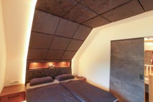 Tischlerei Scharnreitner zeigt ein Schlafzimmer mit extravagentem Akustikpaneel über dem Bett und einem beleuchtetem Ablagefach im Kopfteil.