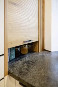 Ein maßgefertigter Rolladenschrank in edler Holzoptik als praktische Küchenaufbewahrungslösung mit sauberer Linienführung von Tischlerei Scharnreitner.