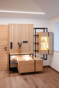 Eine moderne Wohnwand-Kombination mit Vitrine einem modernen Sprossenpaneel als Rückwand und mattschwarzem Eisenrahmen und Ablageflächen von Tischlerei Scharnreitner.