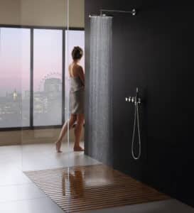 VOLA präsentiert eine große runde Regendusche, eine stabförmige Handdusche und drei Reglern aus mattem Chrom an der Wand montiert.