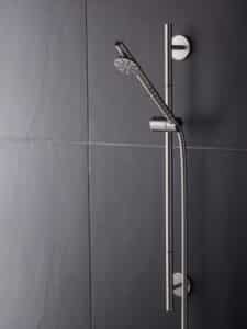 VOLA präsentiert eine stabförmige Kopfdusche mit rundem Düsenaufsatz in mattem Chrom an der Wand montiert.