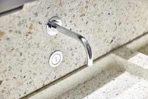 VOLA zeigt die Nahaufnahme einer Waschbecken-Armatur mit Sensor in chrom, die in der Wand integriert ist.