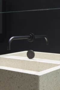 VOLA zeigt die Nahaufnahme einer Waschbecken-Armatur mit Sensor in schwarz, die in der Wand integriert ist.