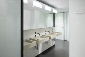 VOLA zeigt die Waschbecken einer öffentlichen WC-Anlage mit schwarzen Armaturen und Sensoren, die in der Wand integriert sind.