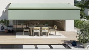 Eine Villa mit Holzdielen im Terrassenbereich und einer fassadenmontierten grünen Markise über den Sitz‑ und Gartenmöbeln mit integrierter Seitenmarkise von Warema.