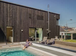 Ein modernes Einfamilienhaus mit Flachdach, dunkler Holzfassade, außenliegendem Schornstein und Pool — nachhaltig gebaut von Weissenseer.