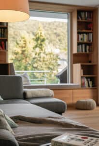 Ein offener Wohnraum mit Couch, Wandverbau und integriertem Sitzfenster von Weissenseer.