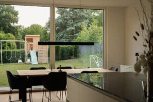 Eine offene Küche mit Esstisch, Terrassenschiebetür und Blick in den Garten mit Spielbereich — warm und familiär gestaltet von Weissenseer.