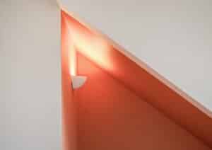 Eine orangene Wand mit Wandbeleuchtung unter der Dachschräge von Weissenseer.