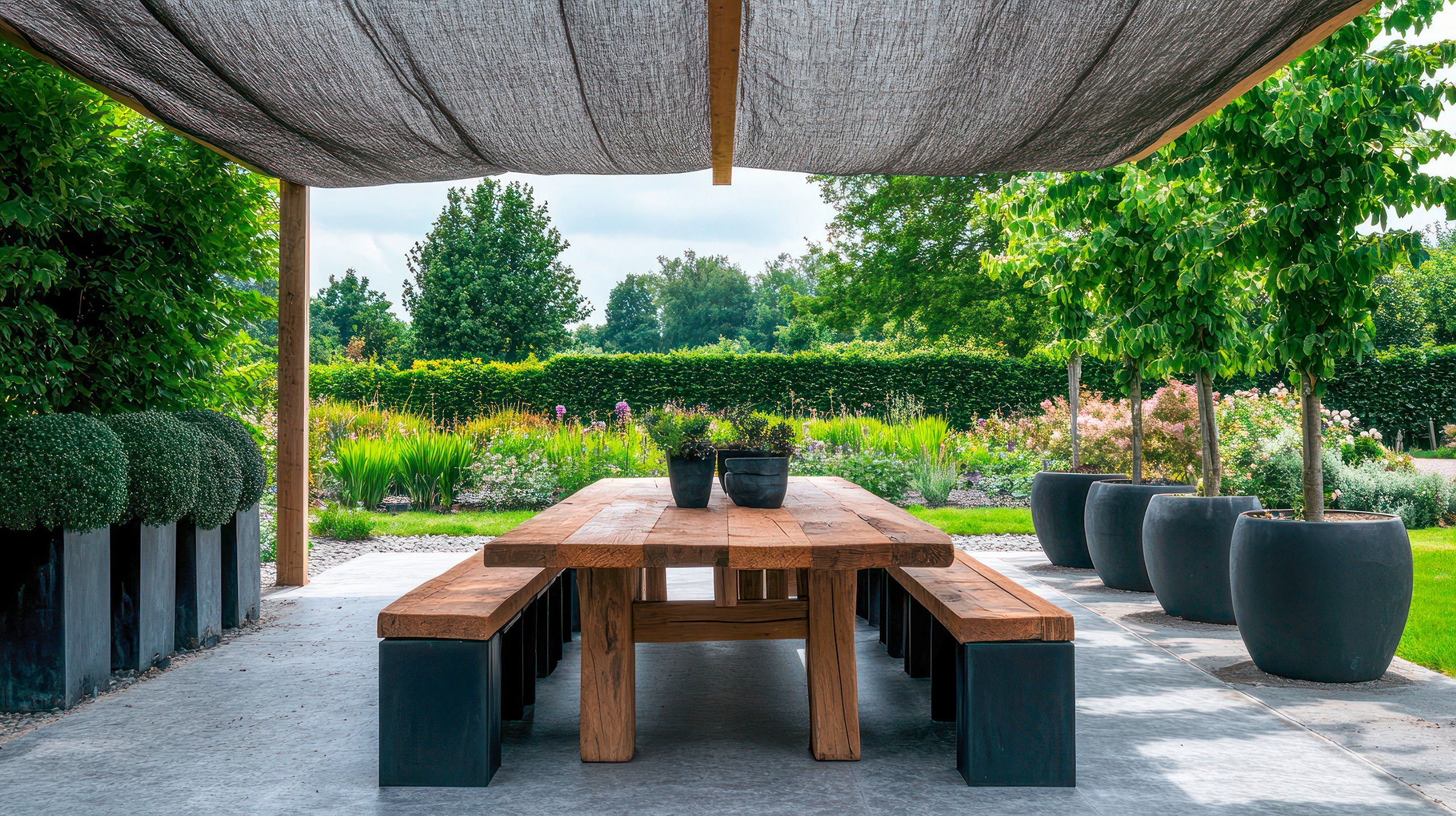 Hölzerner Terrassentisch mit Bänken unter einem Sonnensegel in einem üppigen Garten.