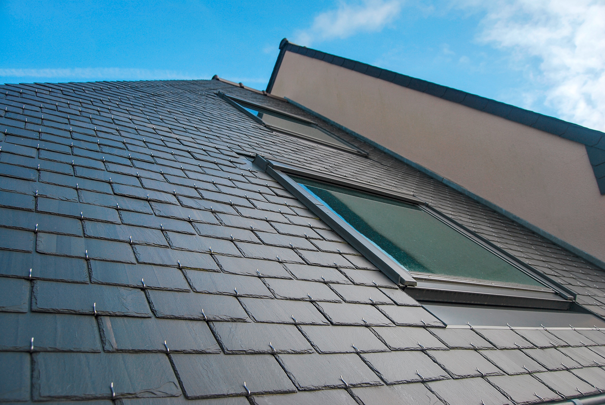 Detailansicht eines modernen Daches mit Dachflächenfenster und hochwertige Dacheindeckung via sichtbar genagelten Schieferschindeln.