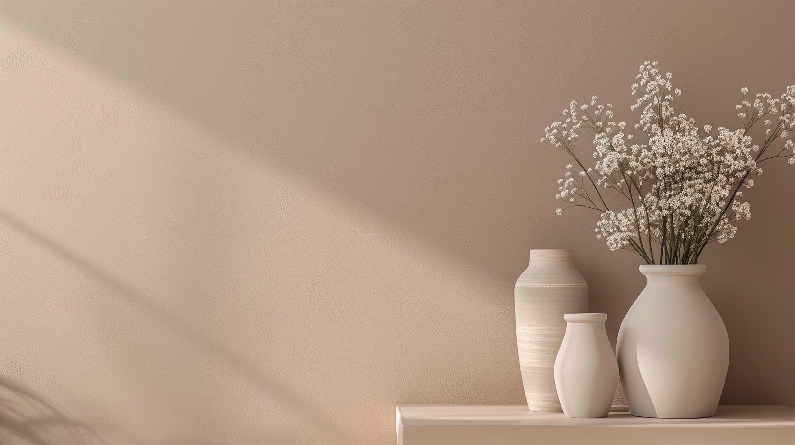 Detailfoto einer Wand in Lachs / Aprikot mit Lichteinfall durch ein Fenster. Auf einem Wandboard sind als Accessoires 3 Vasen in passendem Beigeton platziert. 1 Vase enthält getrocknetes Schleierkraut. - KI-generiert