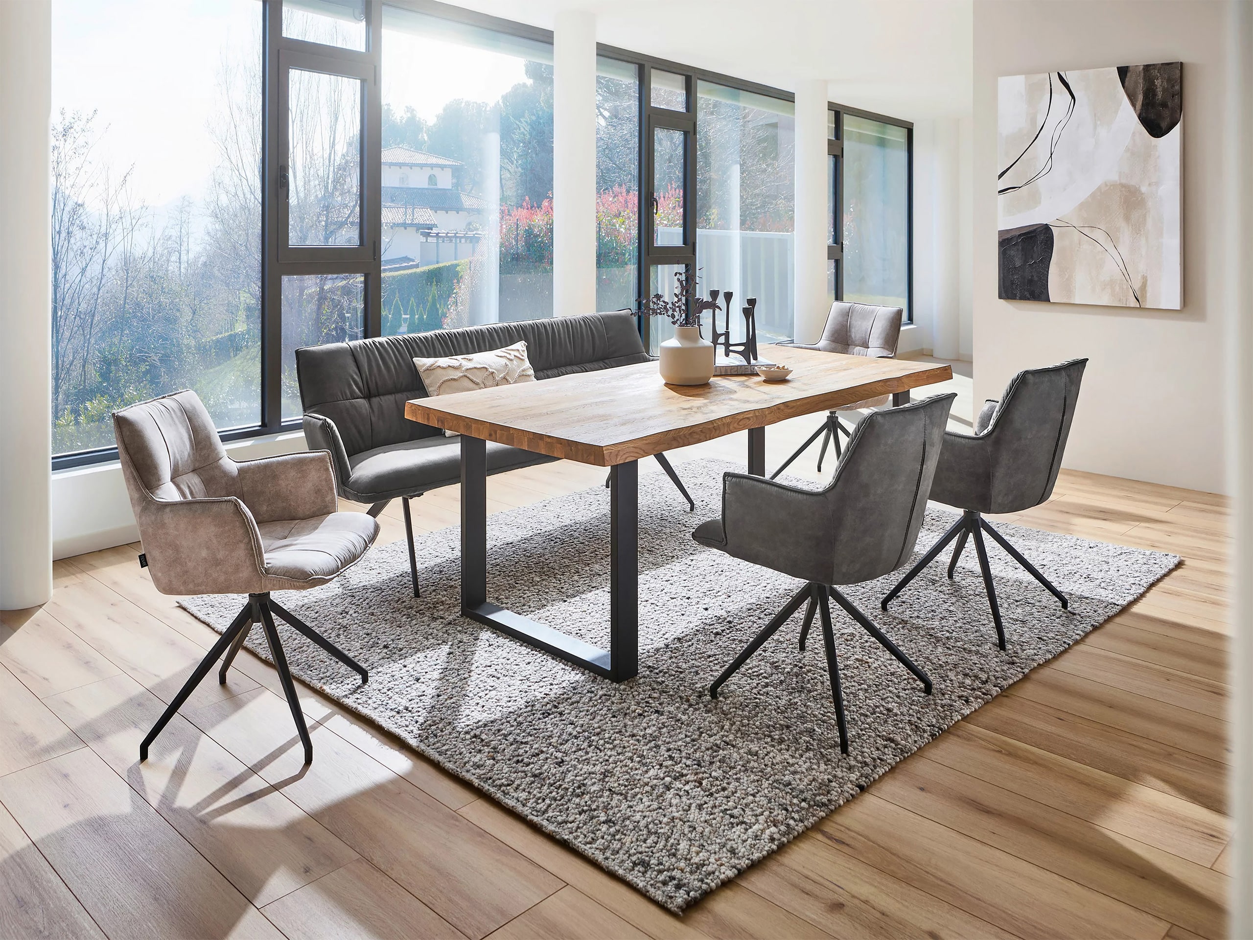 Moderner Essbereich bzw. Esszimmer mit einem Esstisch mit einer massiven Holzplatte mit Naturrandkante, 4 Stühlen in Lederoptik sowie einer gepolsterten Sitzbank mit Rückenlehne. Der Tisch verfüget über ein schwarzes Gestell aus Metall.