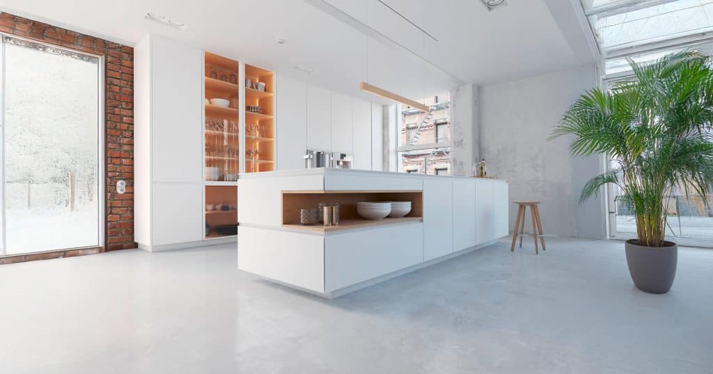 Modernes, offenes Loft mit freistehendem Küchenblock in edlem weiss und dezenter Holzeinfassung der seitlichen Niesche. Weißer Wandverbau mit Glasvitrine im Hintergrund.