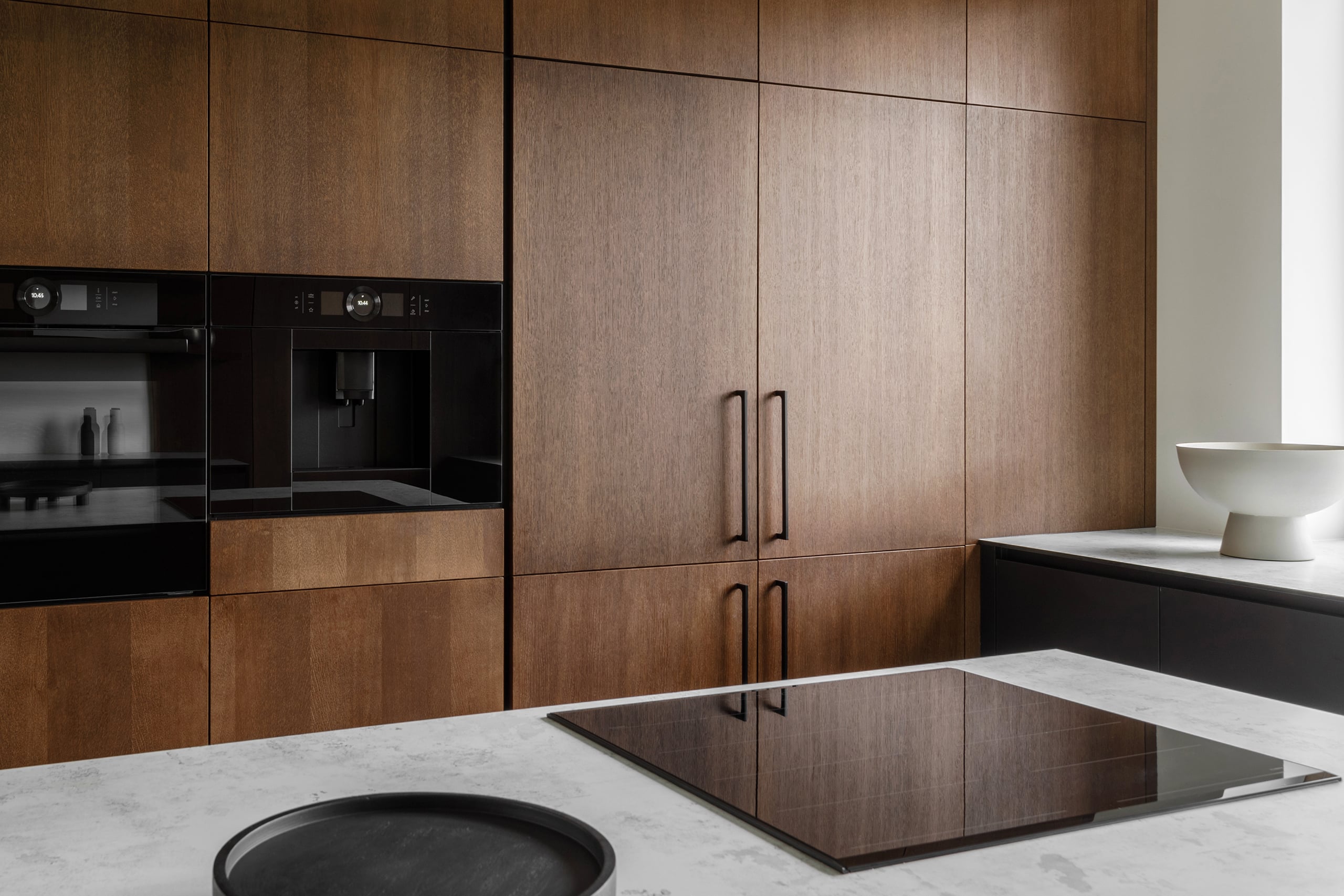 Detailansicht einer modernen Kücheneinrichtung mit Einbaugeräten, wie einem Backrohr und eines Kaffeevollautomaten mit Festwasseranschluss, in ergonomischer Höhe.