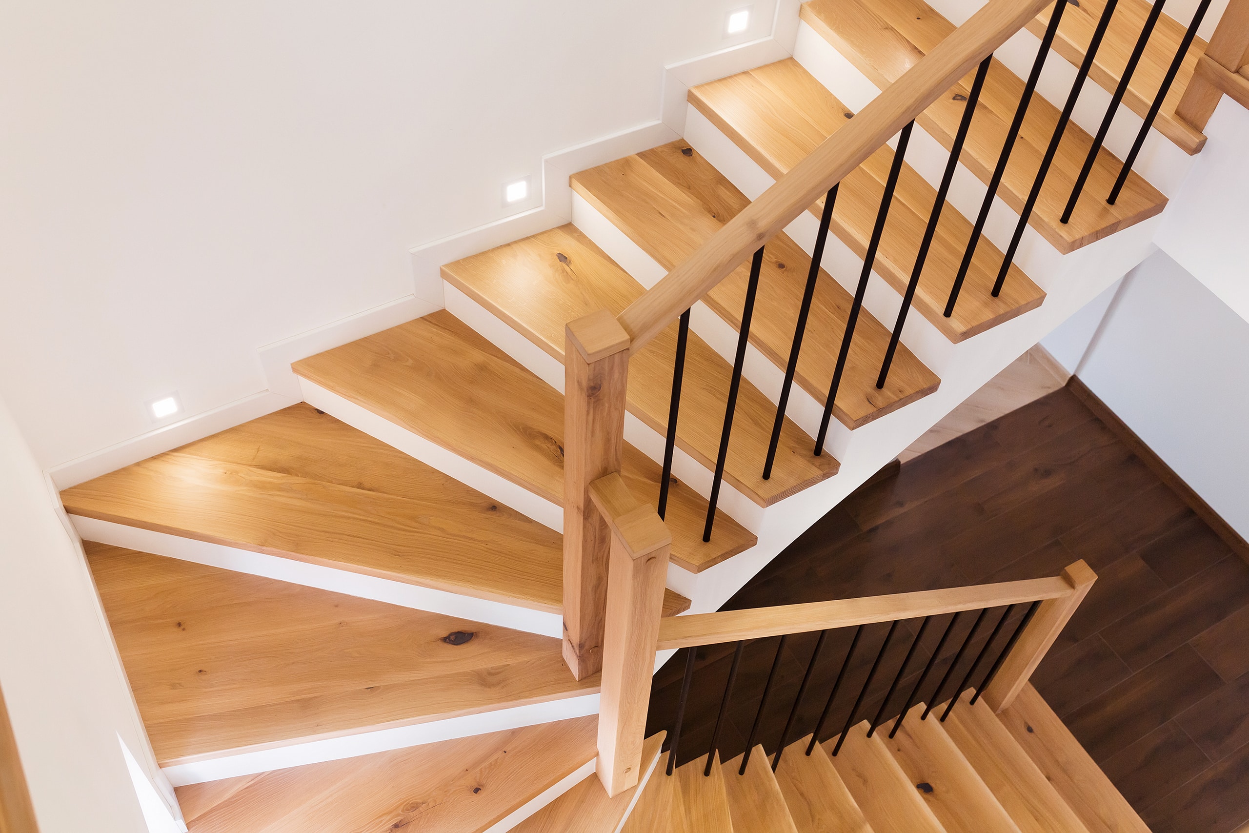 Holztreppe mit weißer Stirnseite und Seitenbereichen mit Geländer aus Holz und schwarzem Metall in einem modernen weißen Haus.