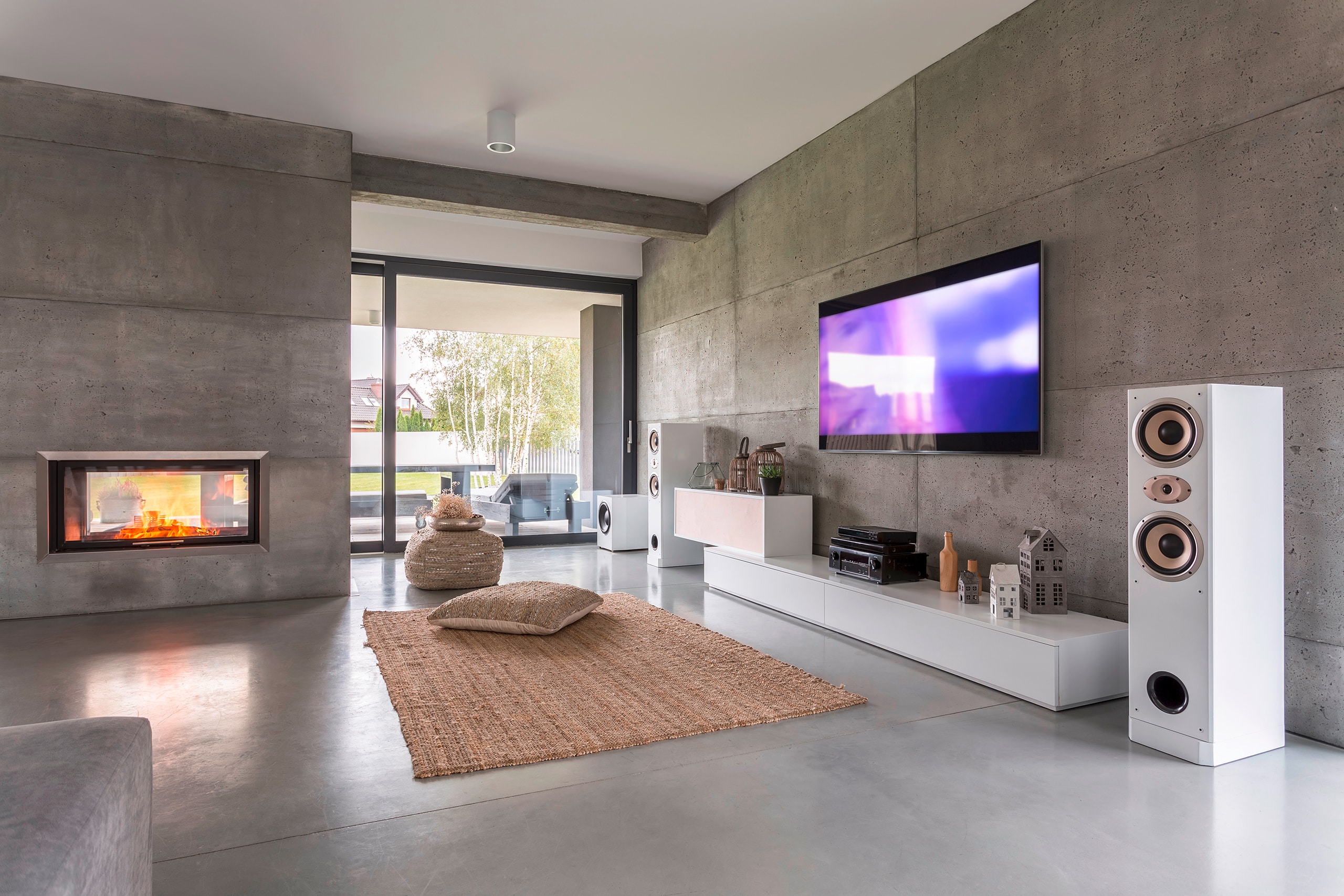 Moderner Wohnraum mit Wänden aus Sichtbeton, Kamin in Sichtbetonwand und beidseitigem Ofenfenster und weißen Sideboards für Multimedia und HiFi-Anlage.