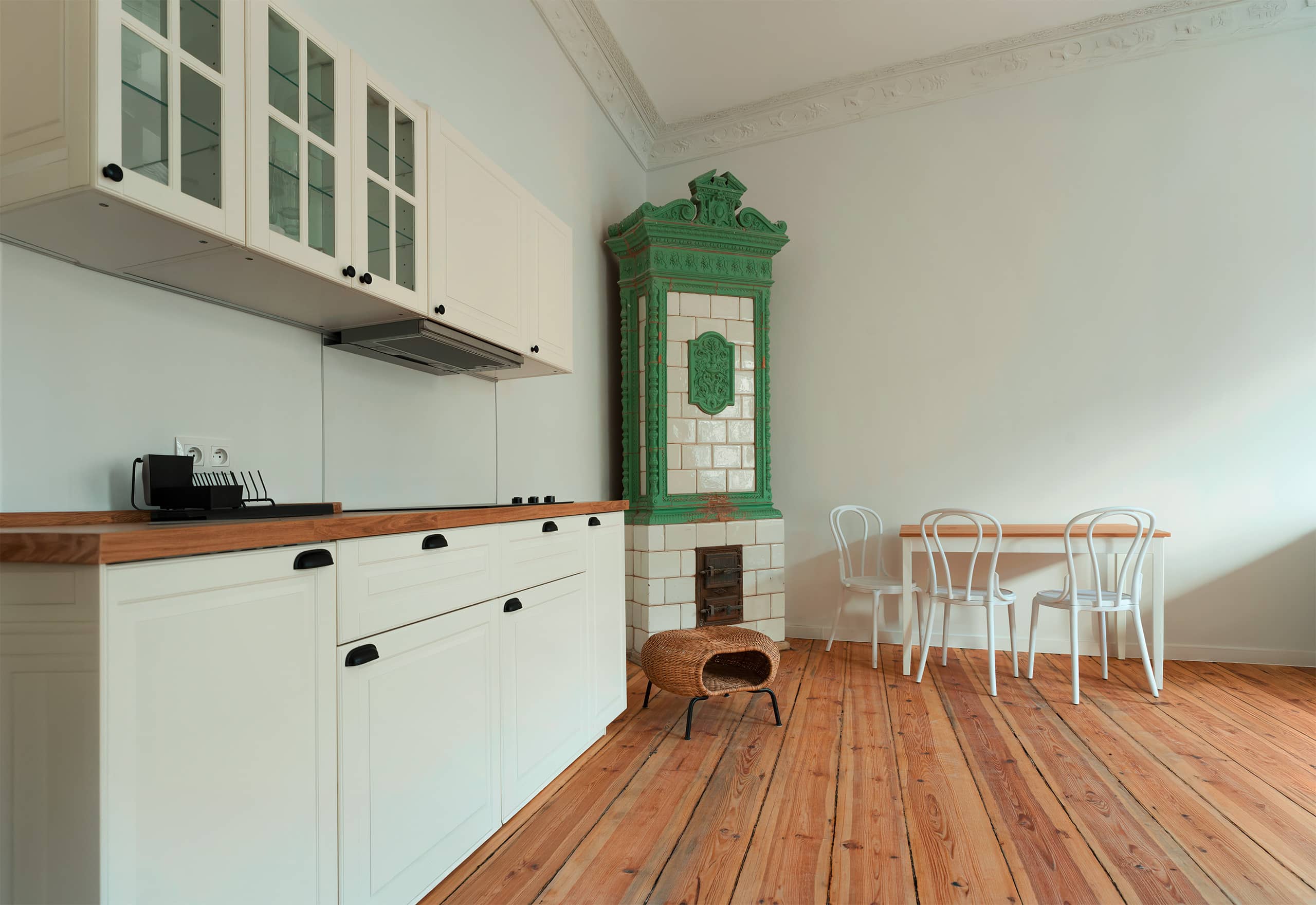 Raumgestaltung im Wohnbereich: Kücheninterieur in einer Loftwohnung mit Ceranherd, Holzboden und Esstisch mit Stühlen und Fokus auf den extravaganten, antiken Kachelofen mit aufwendigem Kacheldesign in kräftigem Grün und Beige.