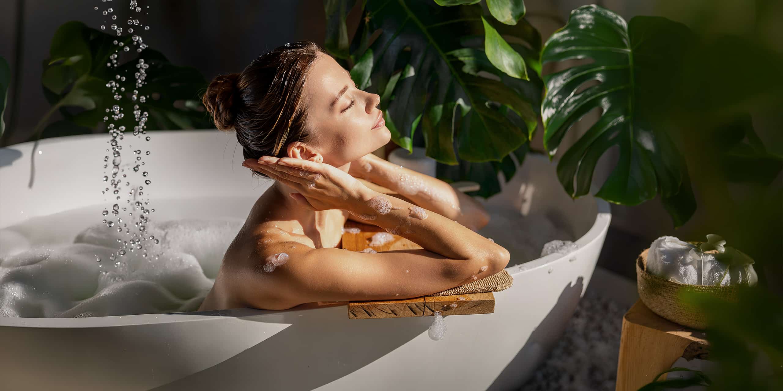 Junge Frau genießt eine entspannte Zeit in der Badewanne mit warmen Wasser und Badeschaum in Ihrem Badezimmer. Umgeben von sanftem, natürlichem Licht und einer entspannenden Atmosphäre mit tropischem Grün. - KI-generiert