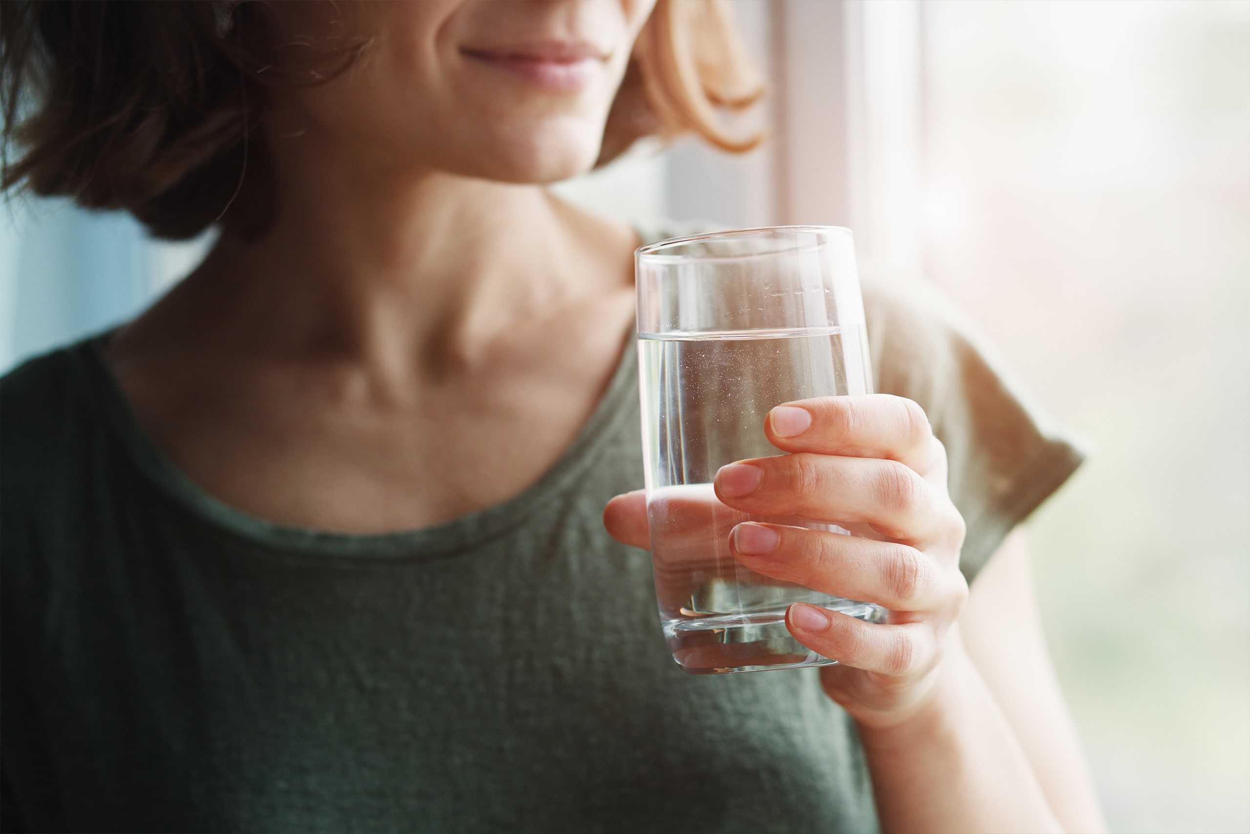 Detailansicht einer junge Frau, die ein Glas Wasser in der Hand Hält. Symbol für die Wichtigkeit des Trinkwassers.