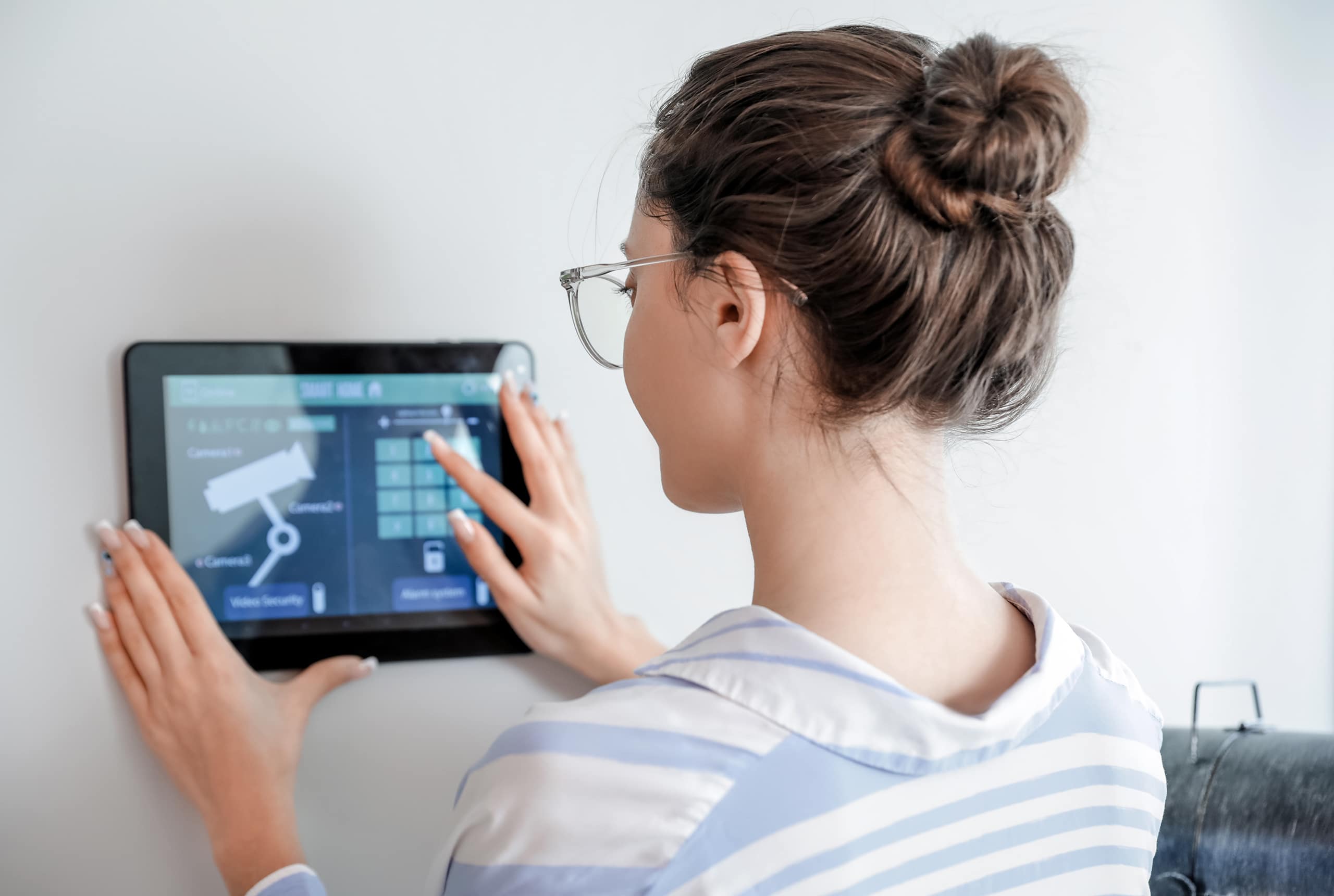 Junge Frau nutzt Bedienfeld eines Smart-Home-Sicherheitssystems und nimmt Einstellungen an der Überwachungskamera vor.