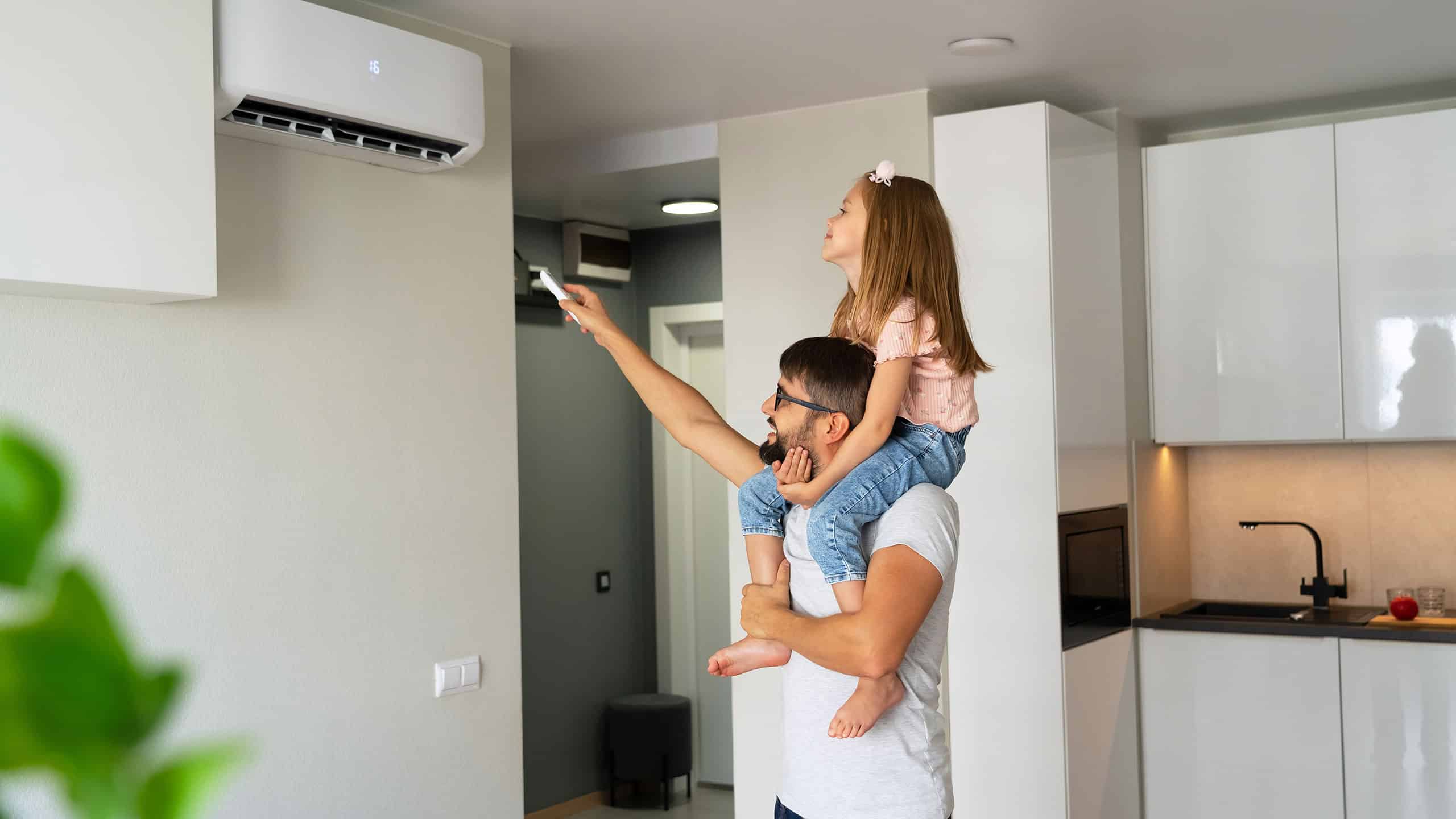 Vater mit seiner kleinen Tochter auf den Schultern schaltet das Splitgerät einer Klimaanlage per Fernbedienung ein und kühlt so den Raum nach gewünscht definierter Temperatur.